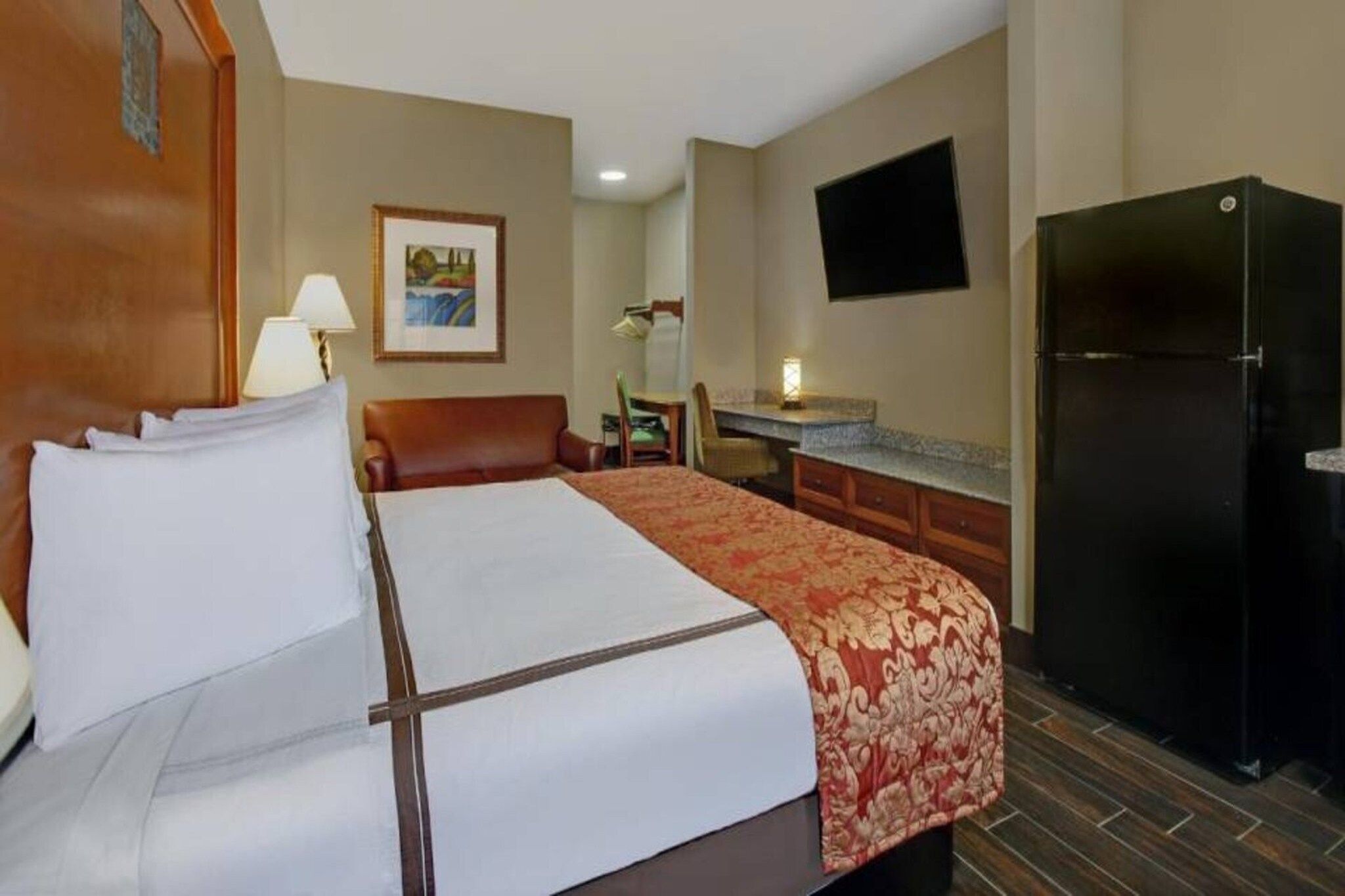 Habitación de hotel con cama, escritorio, silla, televisor y refrigerador.