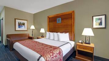 Une chambre d’hôtel avec un grand lit, deux tables de chevet avec des lampes, un fauteuil en cuir marron et deux tableaux encadrés accrochés aux murs.