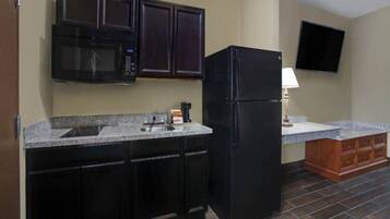 A kitchen with dark cabinets, a black refrigerator, a microwave, and a flat-screen TV mounted on the wall.