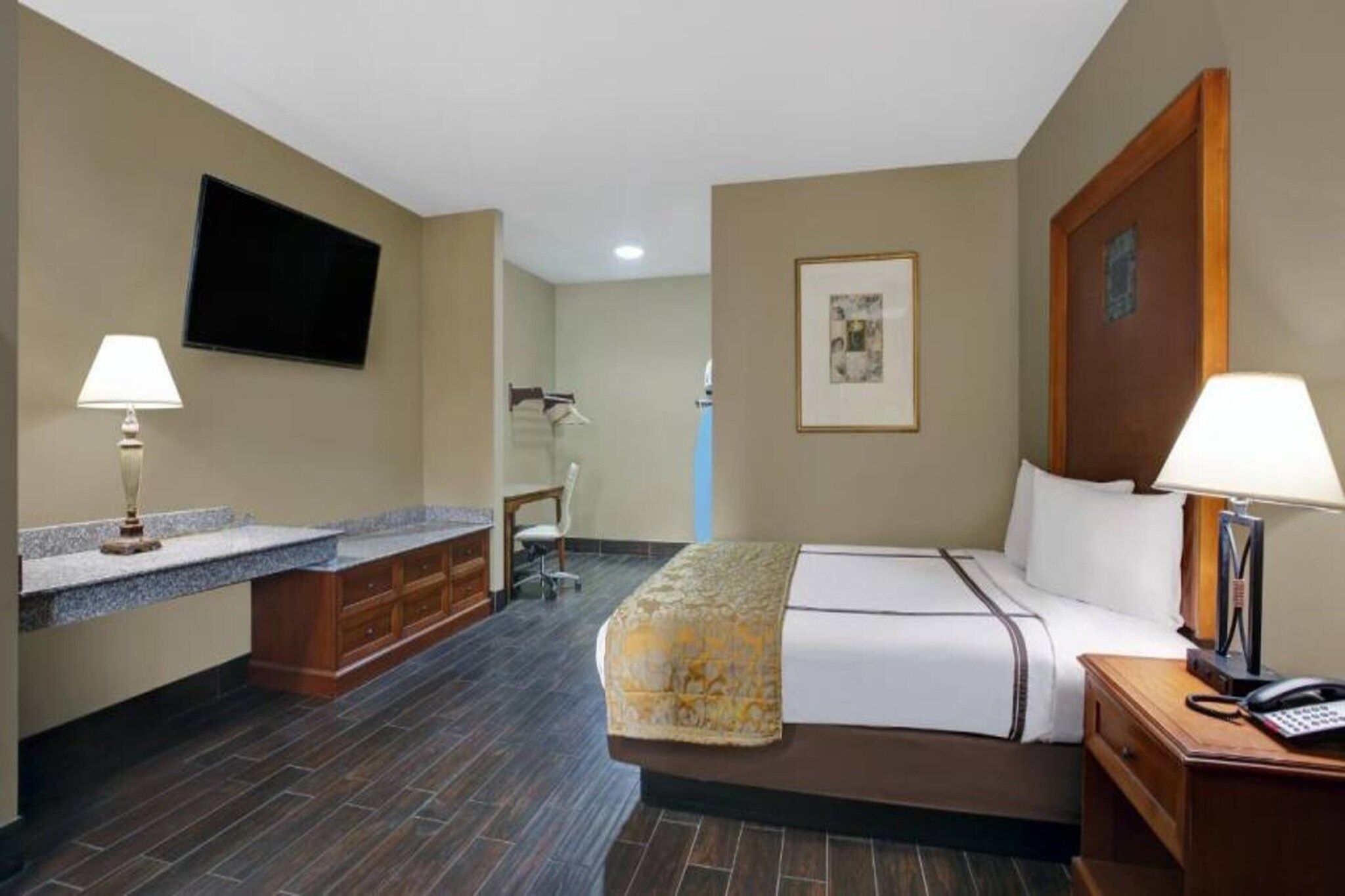 A hotel room with a bed, bedside table, lamp, desk, chair, and a flat-screen TV mounted on the wall.