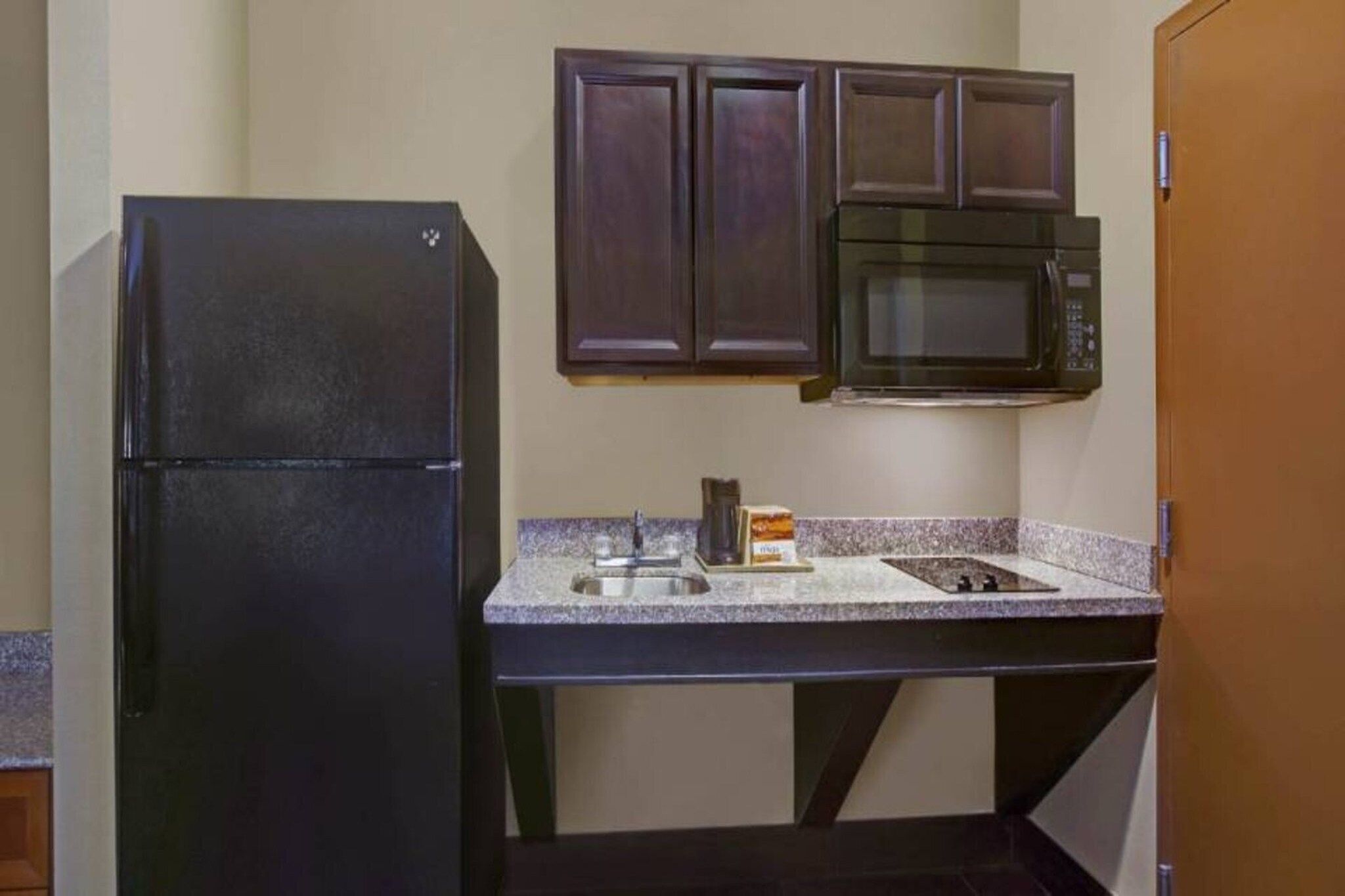 Una cocina compacta con un refrigerador negro, un microondas y una encimera de granito.