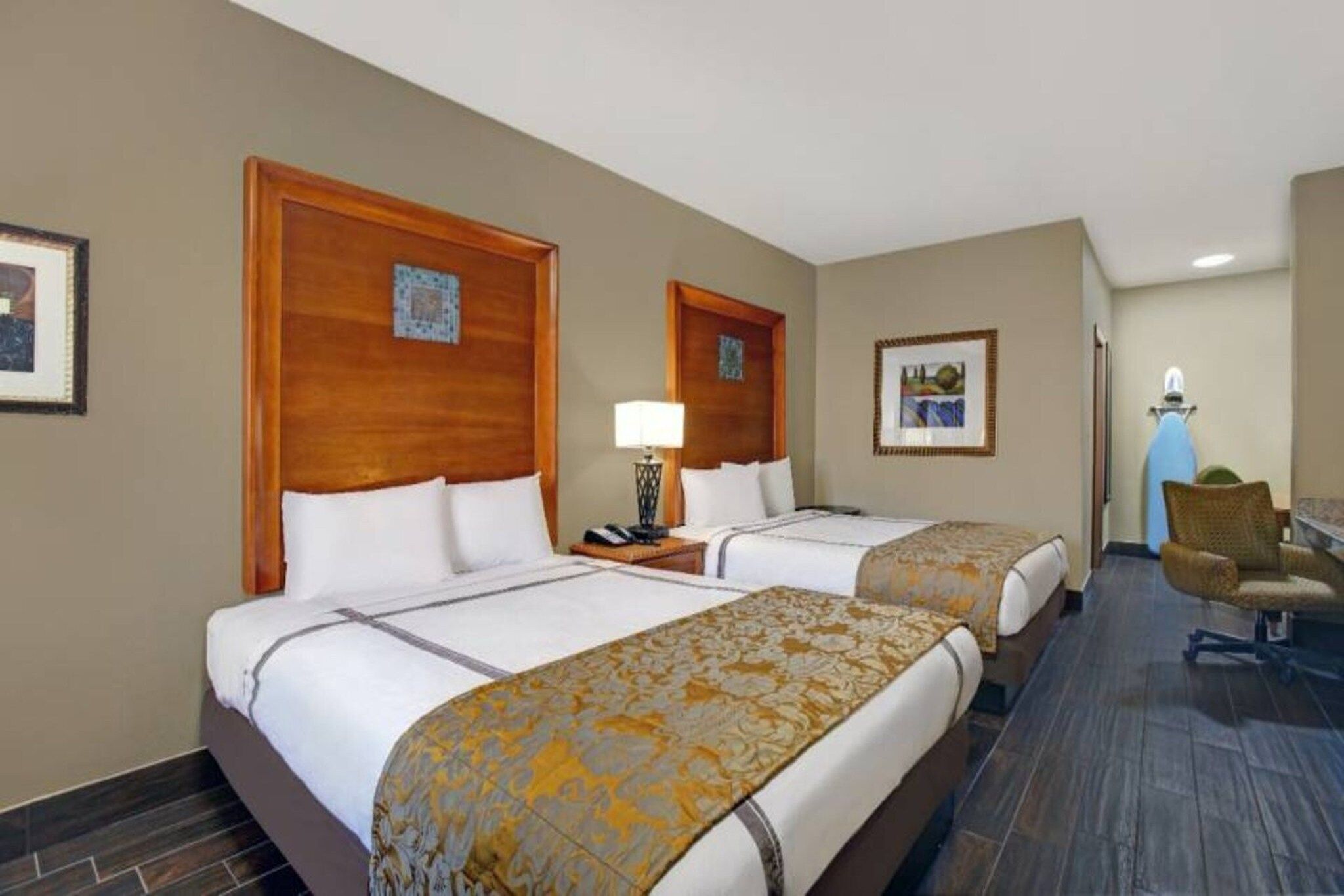 Een hotelkamer met twee bedden, een bureau, een stoel en kunstwerken aan de muur.