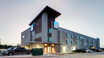 A modern hotel with a flat roof, multiple windows, and a parking lot with several cars.