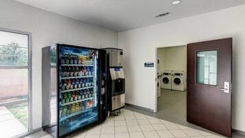 A vending machine and a washer-dryer unit in a room with tiled flooring and a door leading to another area.
