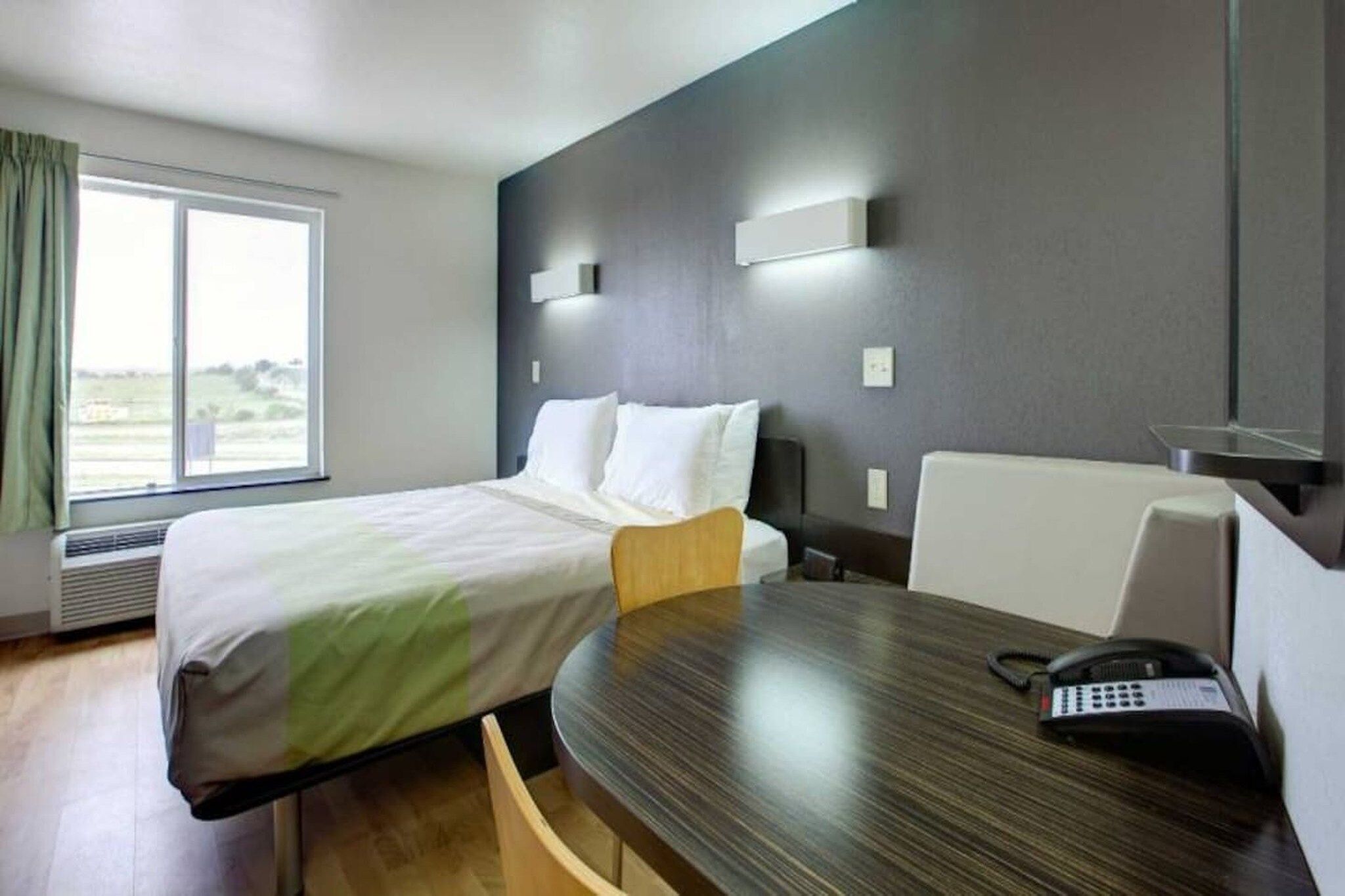 Een hotelkamer met een bed, een bureau met telefoon en een raam met gordijnen.
