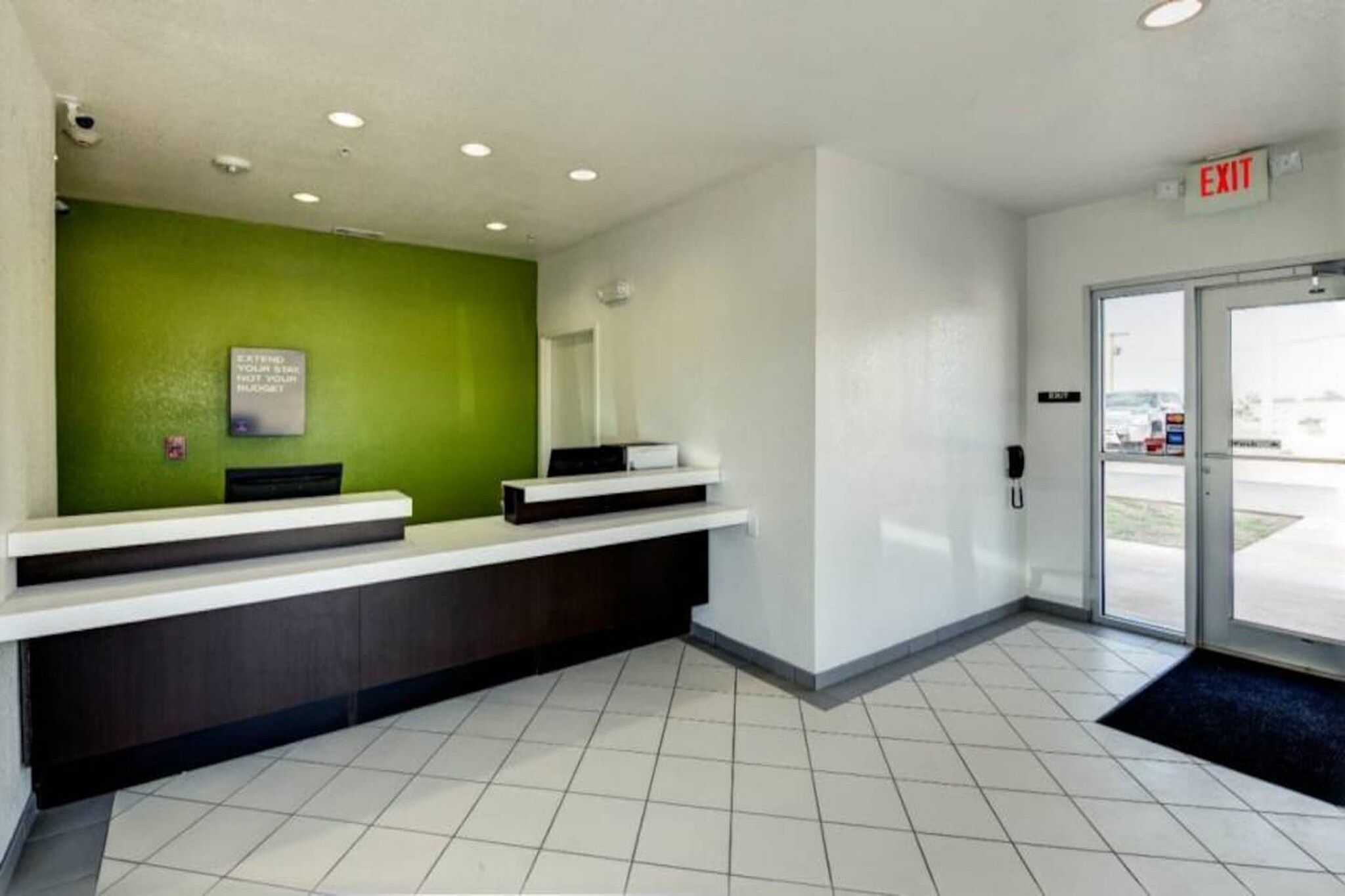 A reception area with a green wall, two reception counters, a white tiled floor, and an exit sign.