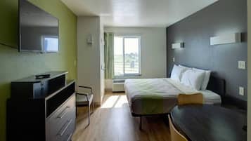 Et hotelværelse med seng, skrivebord, fjernsyn og et vindue med gardiner.