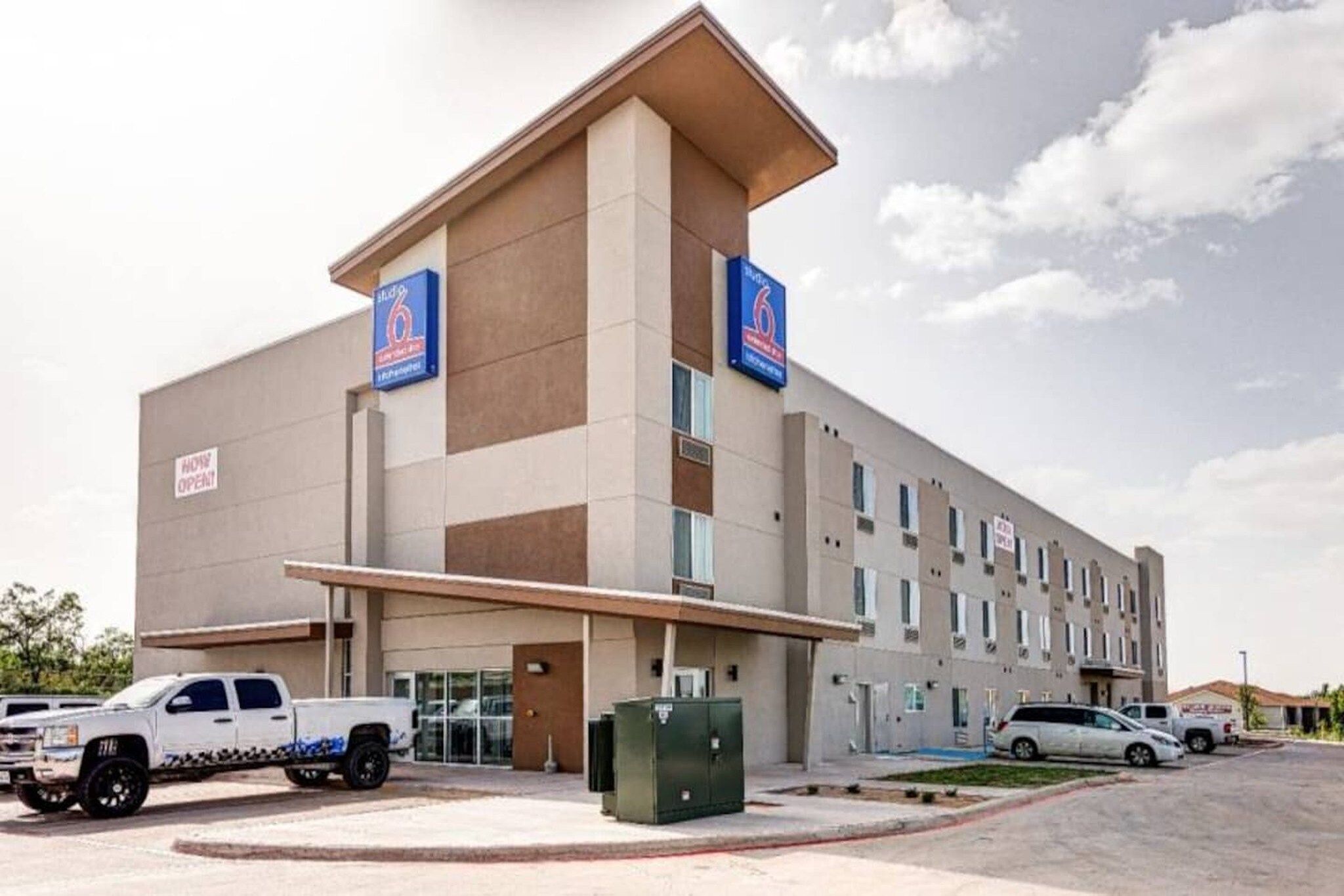 A multi-story hotel with a flat facade, a parking lot, and a clear sky.
