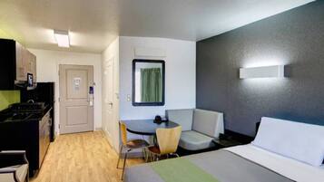A hotel room with a bed, a desk with a chair, a small kitchenette, and a window with curtains.