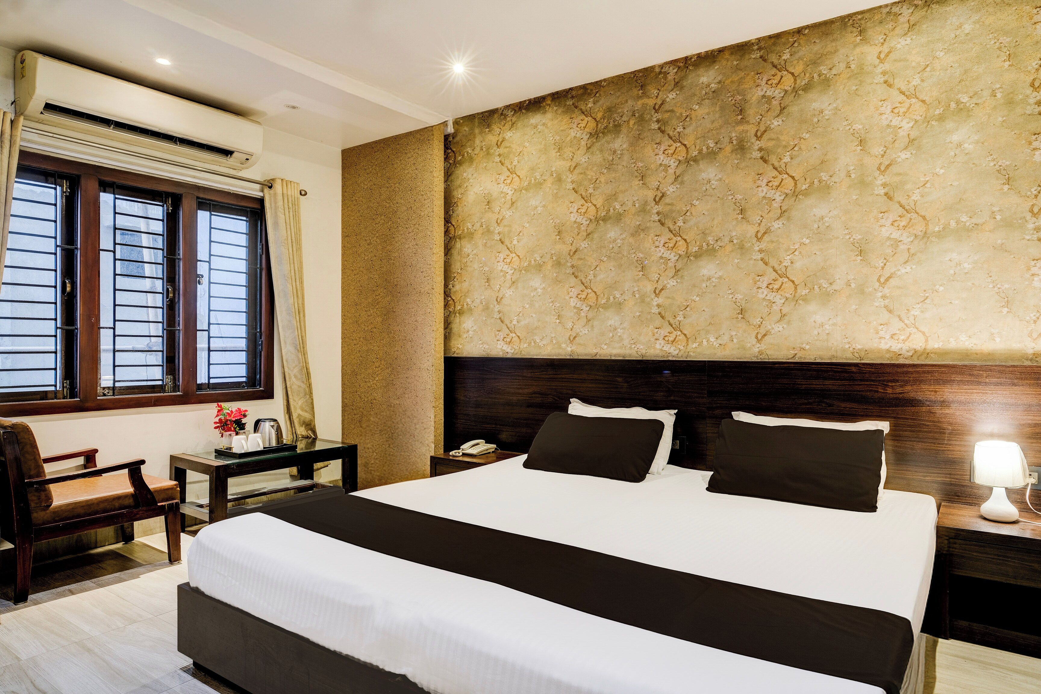 A hotel room with a large bed, a nightstand, a desk, and a window with curtains.