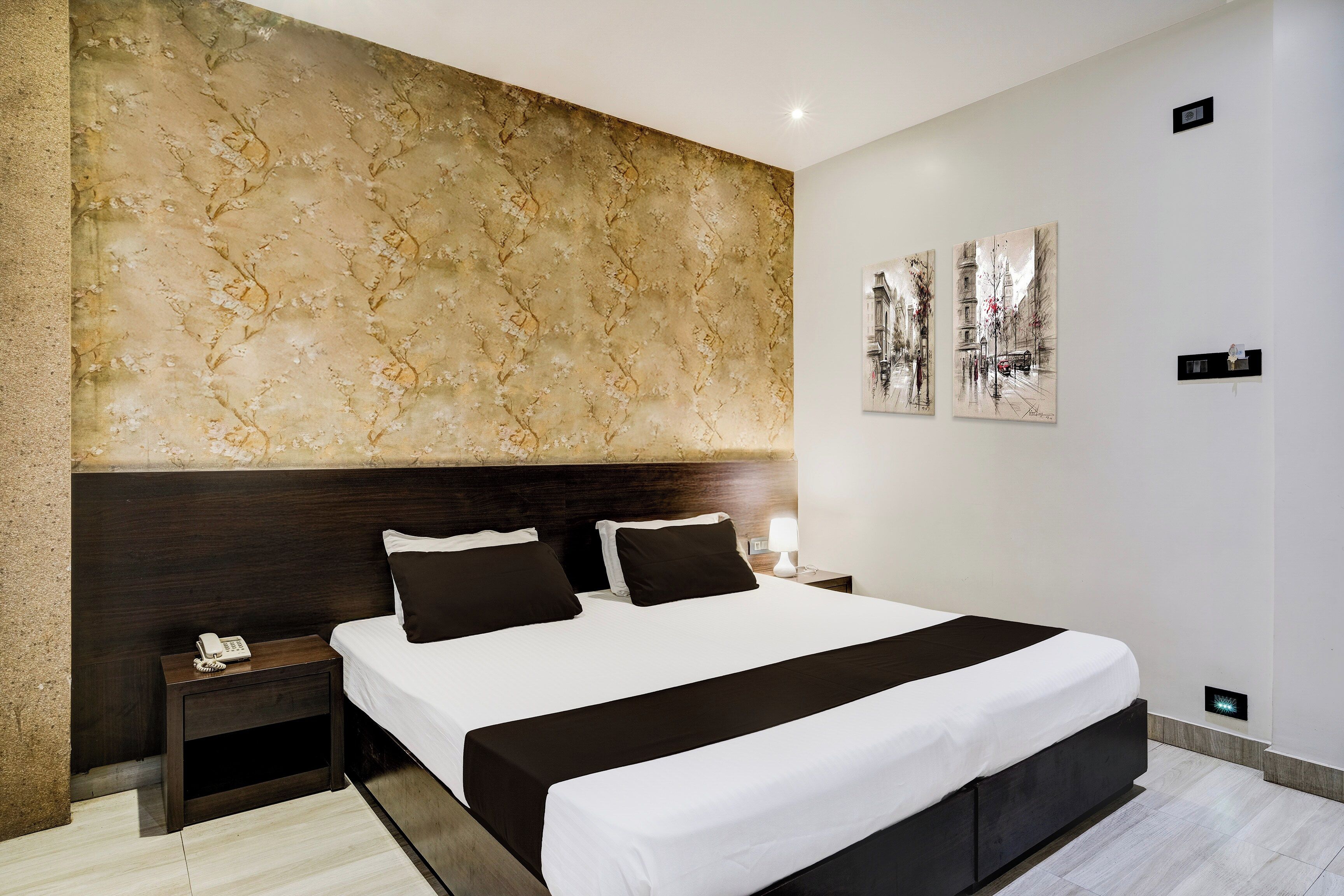 Une chambre d’hôtel moderne avec un grand lit, une tête de lit en bois foncé, une table de chevet avec un téléphone et une lampe fixée au mur.
