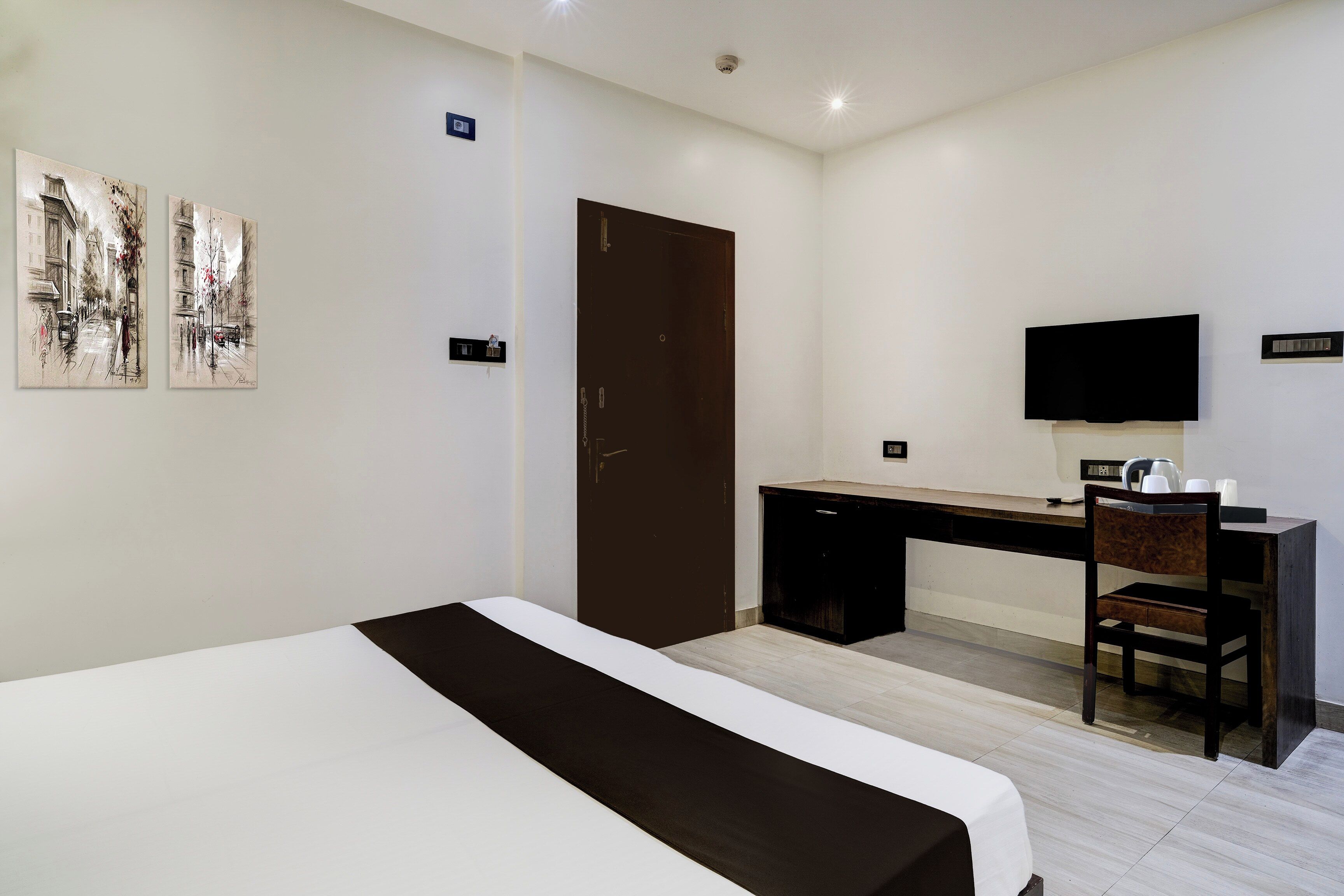 Ein Hotelzimmer mit Bett, Schreibtisch, Stuhl, Fernseher und einem Kunstwerk an der Wand.