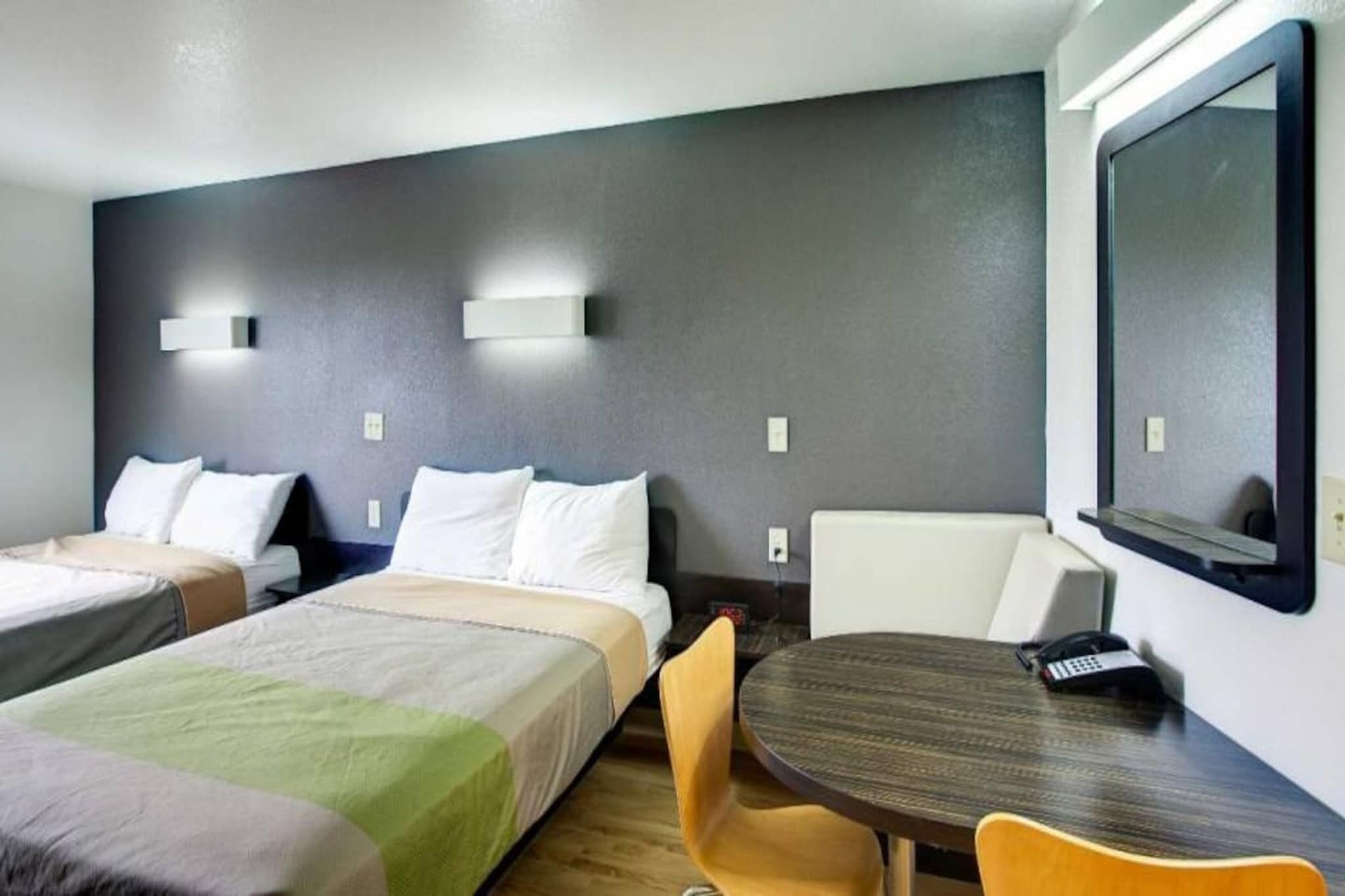 A hotel room with two beds, a round table, and a chair.