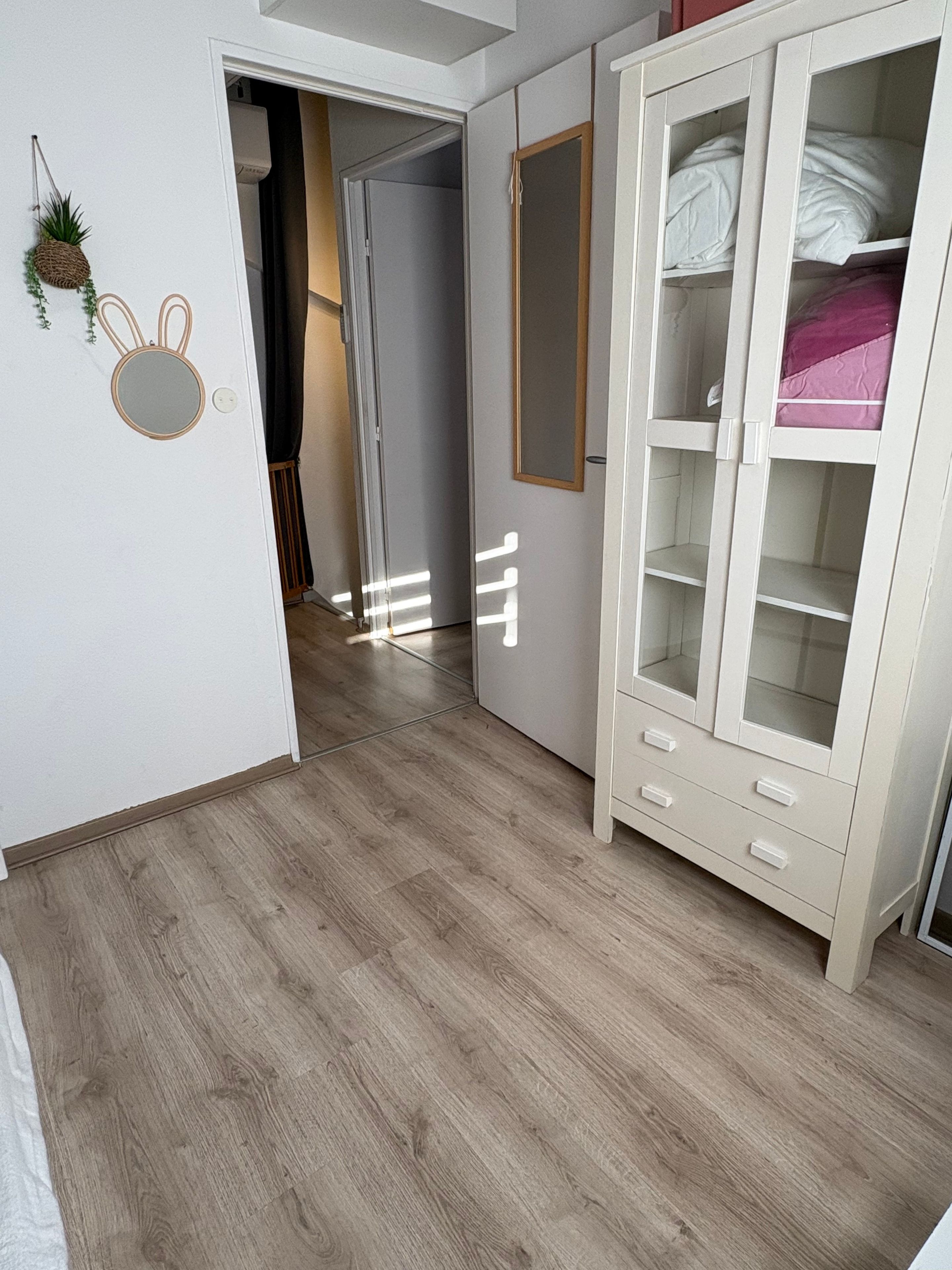 A bedroom with a wardrobe, a mirror, and a door leading to another room.