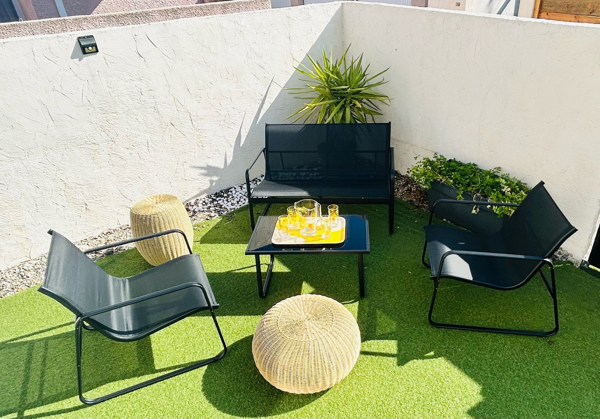 An outdoor seating area with two black chairs, a small table with drinks, and a potted plant.