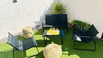 An outdoor seating area with two black chairs, a small table with drinks, and a potted plant.
