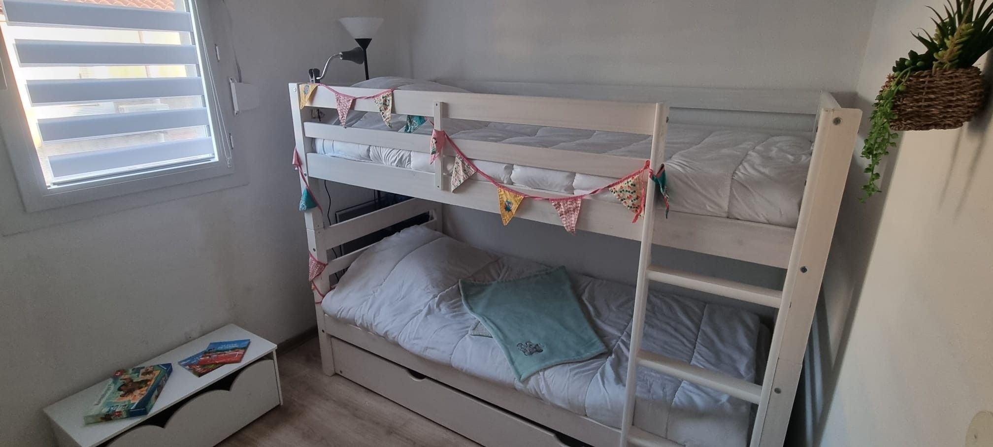A bunk bed with a small bedside table and a window with blinds.