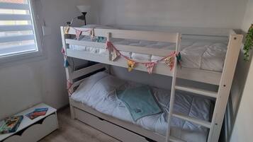 A bunk bed with a small bedside table and a window with blinds.