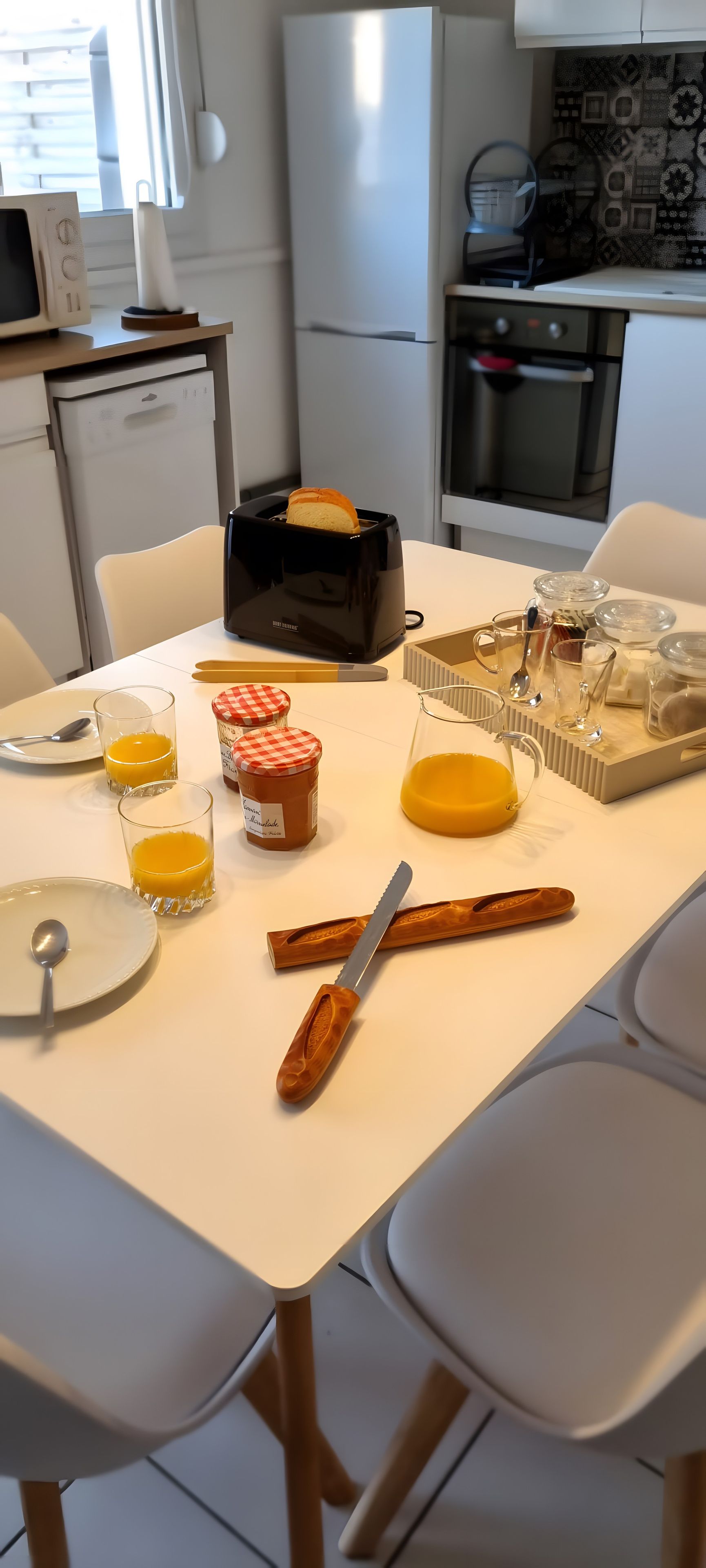 Una mesa de desayuno con un tostador, vasos de zumo de naranja, un cuchillo y un tarro de miel.