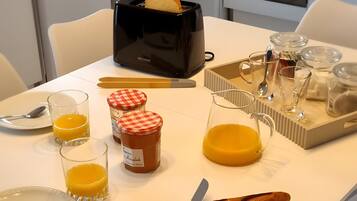 Una mesa de desayuno con un tostador, vasos de zumo de naranja, un cuchillo y un tarro de miel.