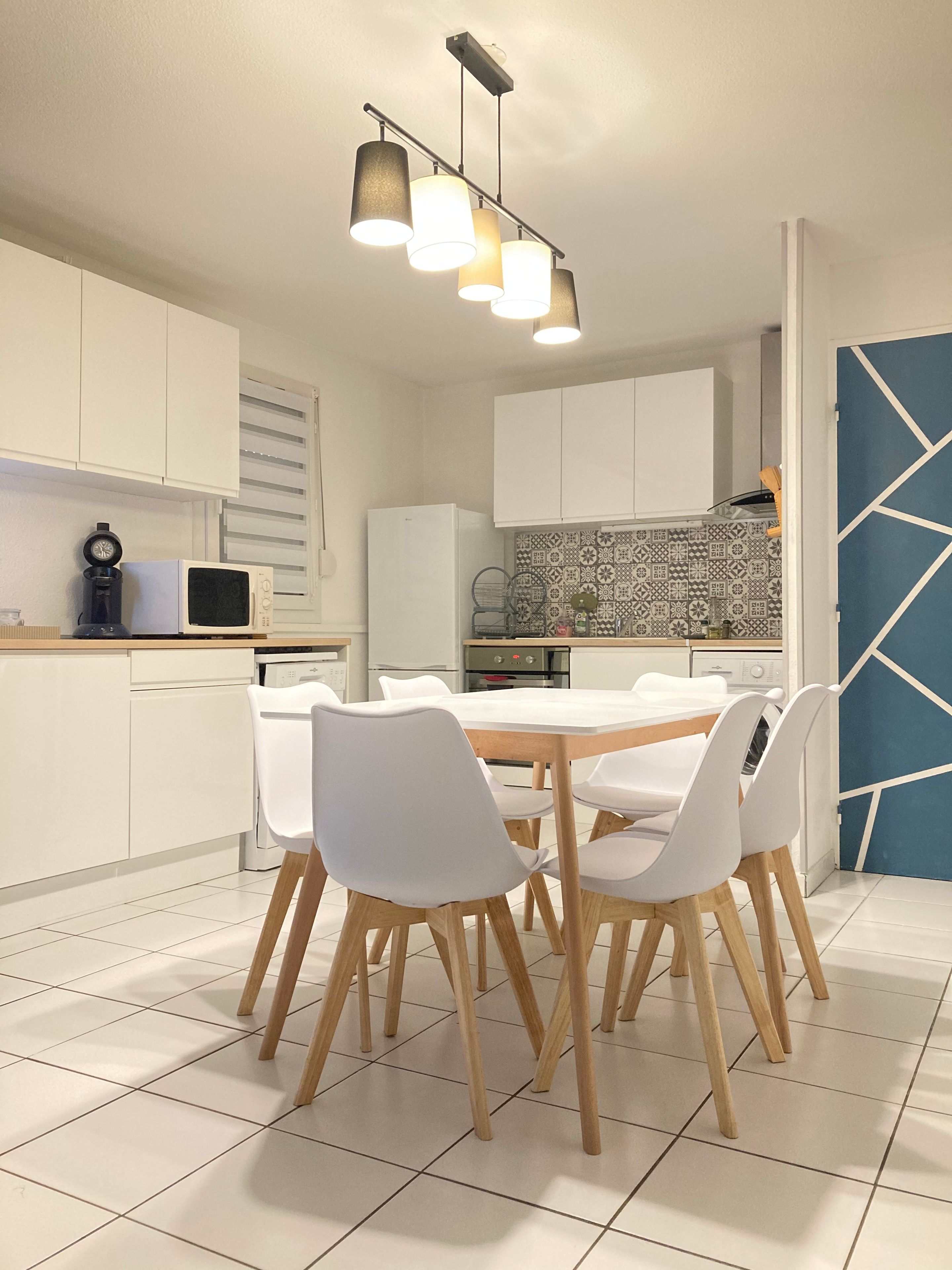 Eine moderne Küche mit weißen Schränken, einer gefliesten Spritzschutzwand und einem Essbereich mit weißem Tisch und Stühlen.