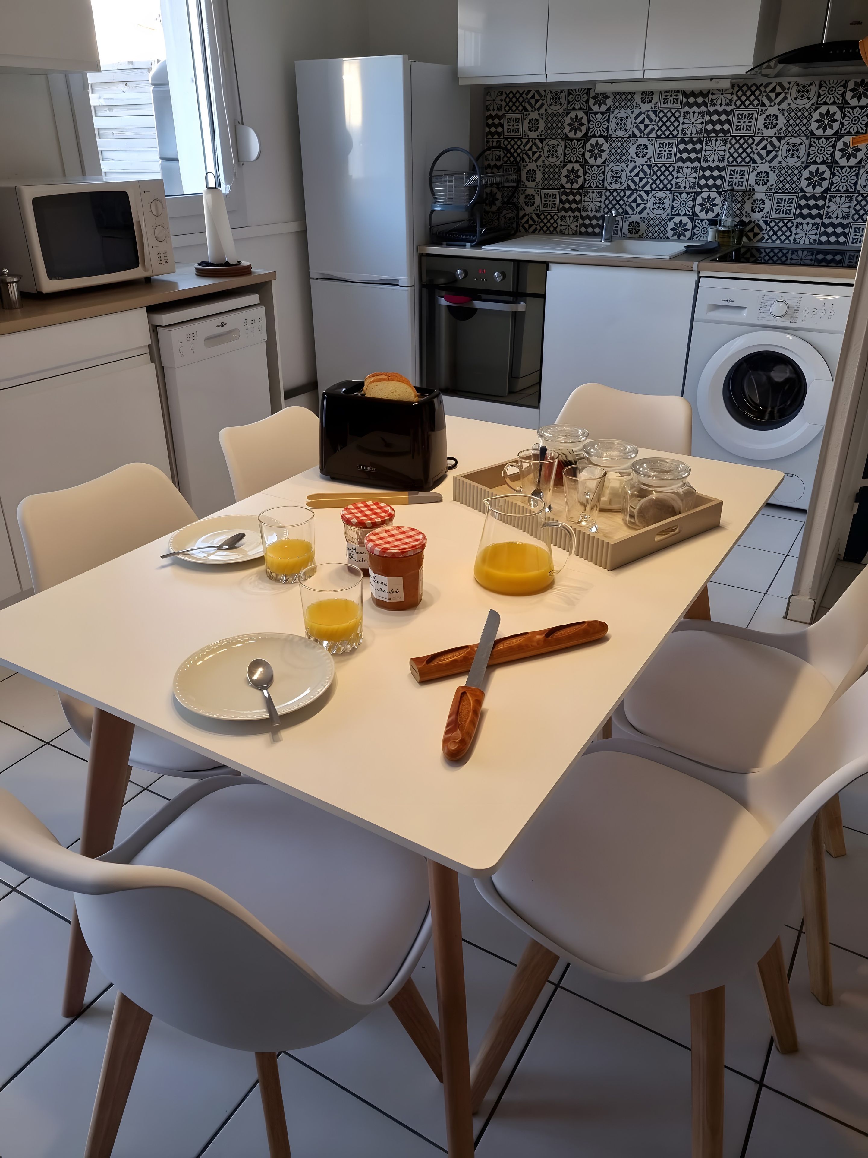 A modern kitchen with a dining table set for two, equipped with a toaster, a kettle, and a microwave.