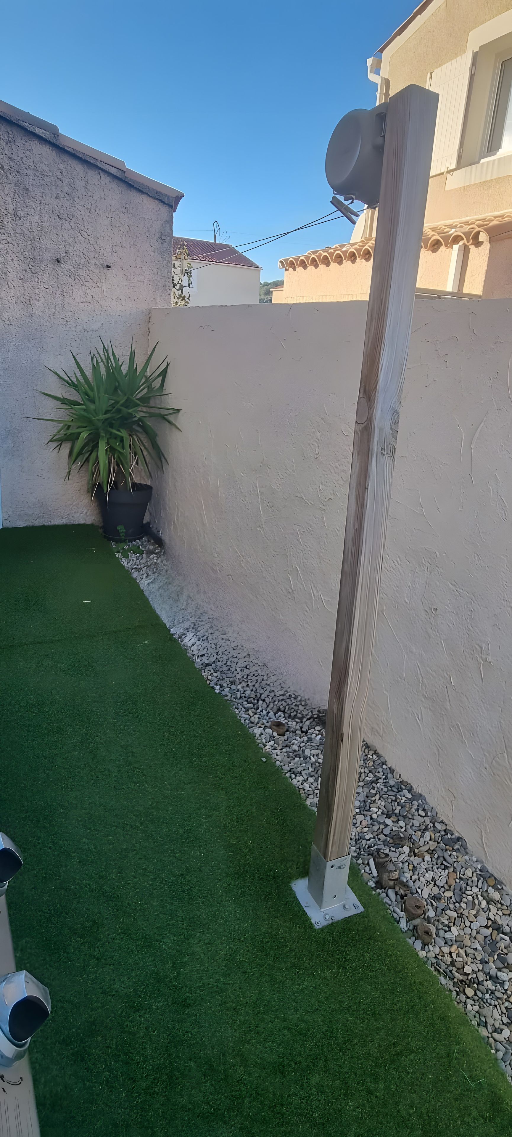 Ein Garten mit Kunstgrasanlage, einem Blumentopf und einem Holzpfosten.
