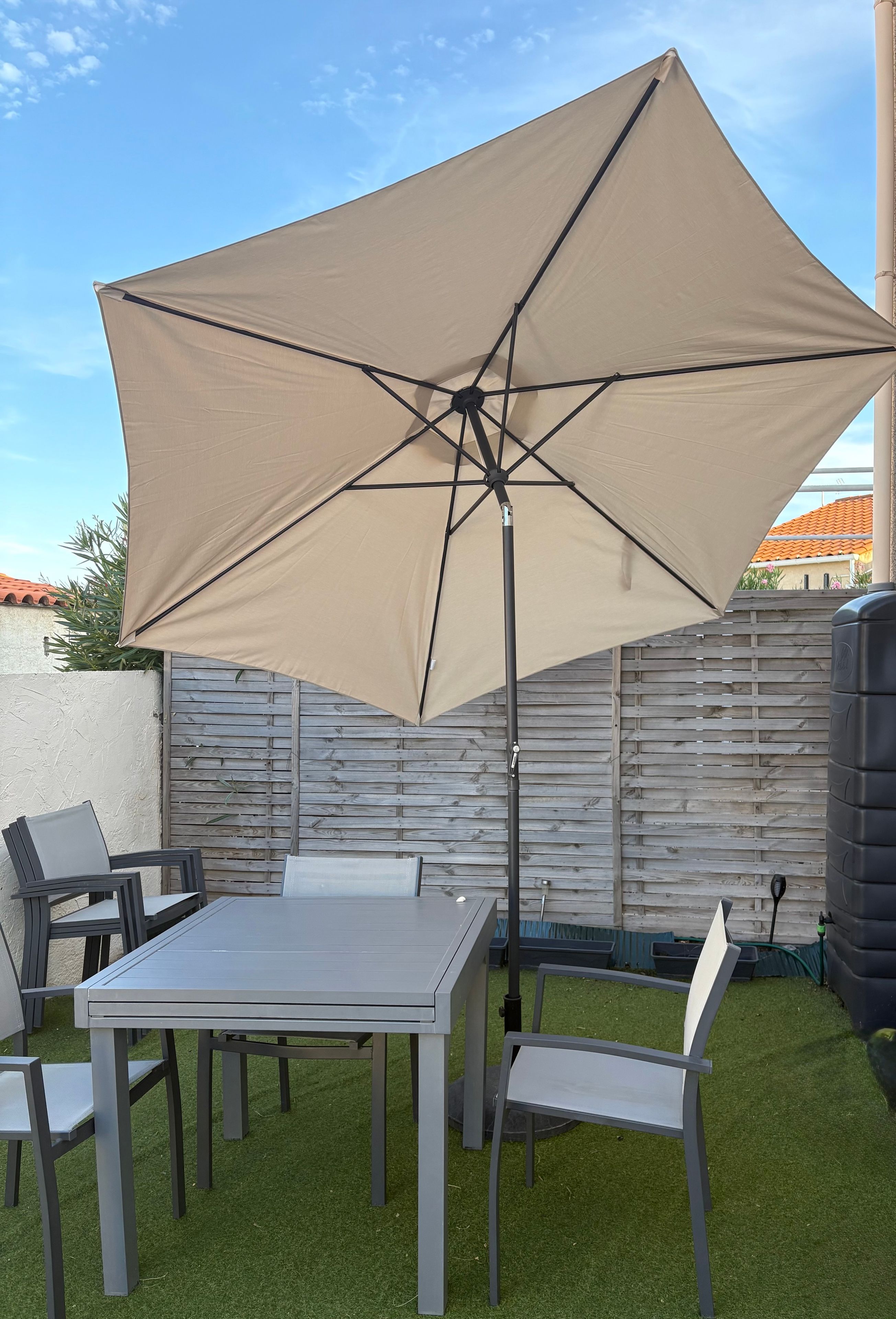 Une terrasse extérieure avec une table et des chaises, un grand parasol et une clôture en bois en arrière-plan.