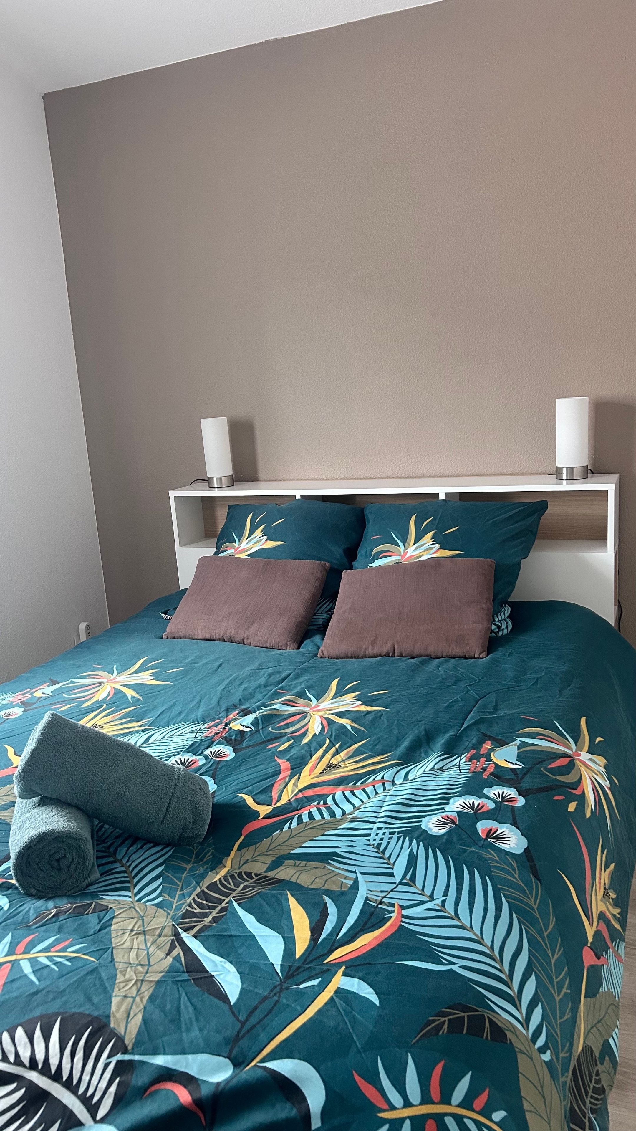 Ein Bett mit einer blumigen Bettdecke, zwei Kissen und einem zusammengerollten Handtuch.