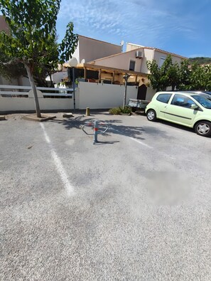 Un espace de stationnement avec une voiture, un arbre et un bâtiment doté d’un mur blanc et d’antennes paraboliques.