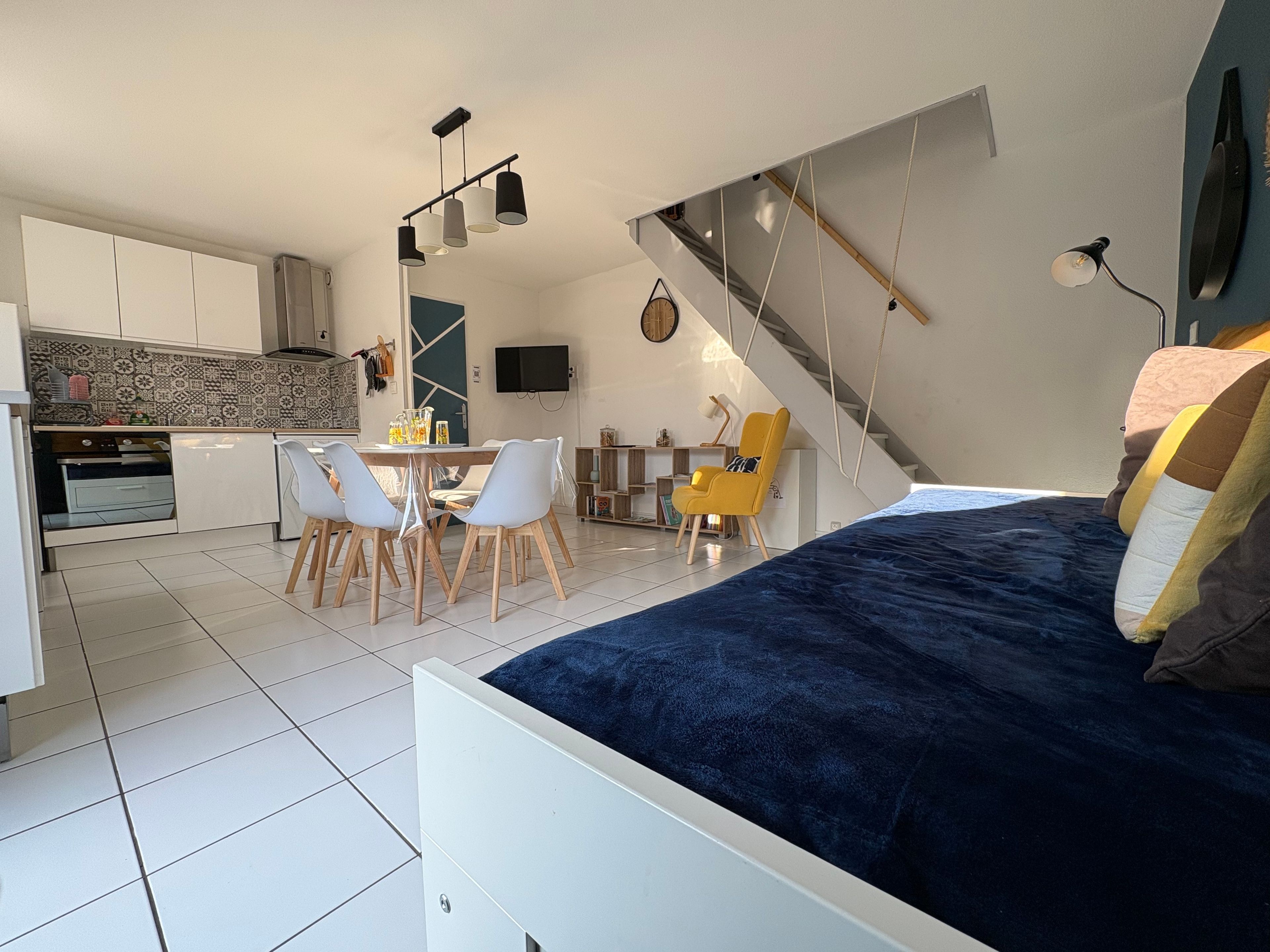 Un espace de vie compact comprenant un lit, un coin repas, une cuisine et un escalier.