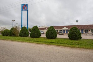 A motel with a prominent blue sign, a parking lot, and a building with a brown roof. - 2 Full Beds | Smoking, Micfridge (Madisonville)