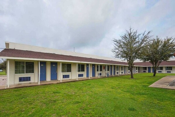 A row of motel buildings with individual rooms, a grassy lawn, and a tree. - 2 Full Beds | Smoking, Micfridge (Madisonville)