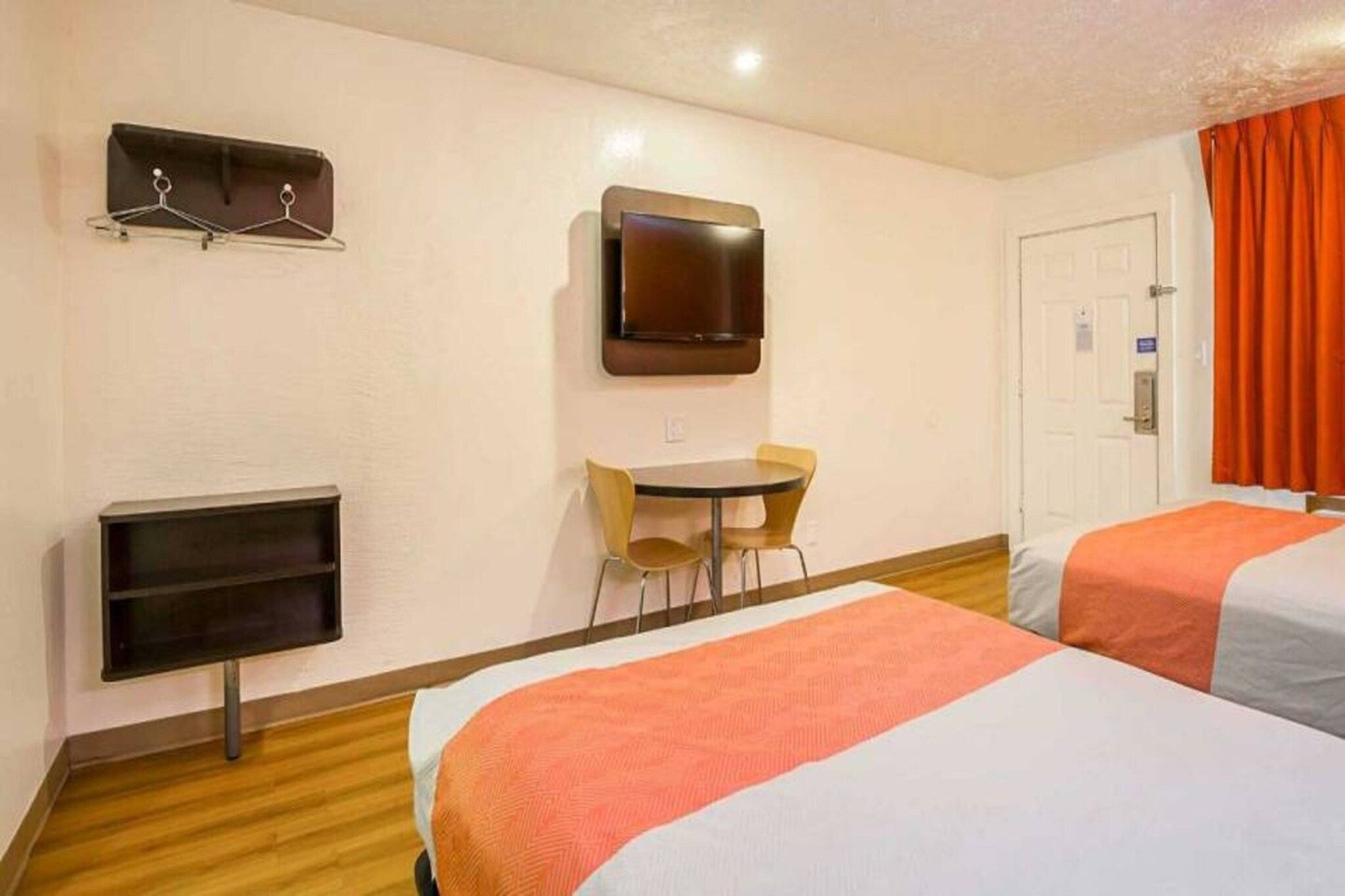 A hotel room with two beds, a desk, a chair, a TV, and a coat rack.
