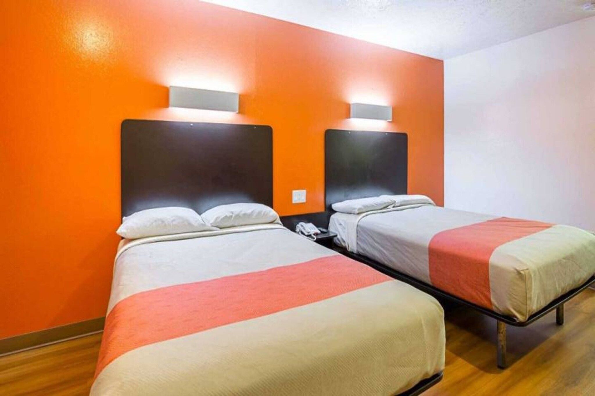 A hotel room with two beds, each with a headboard and bedside lamps.