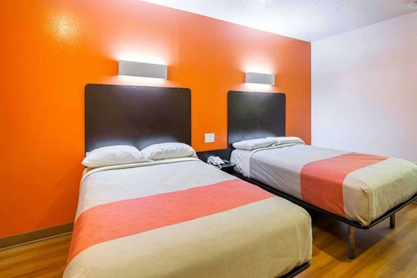 A hotel room with two beds, each with a headboard and bedside lamps.