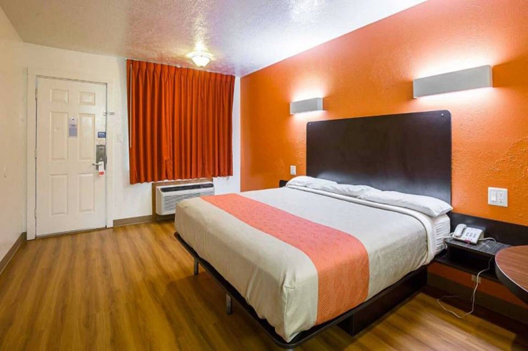 A hotel room with a bed, a desk, a telephone, and a door.