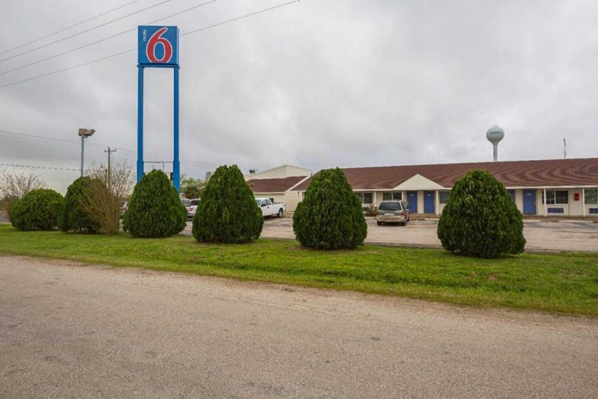 A motel with a prominent blue sign, a parking lot, and a building with a brown roof.
