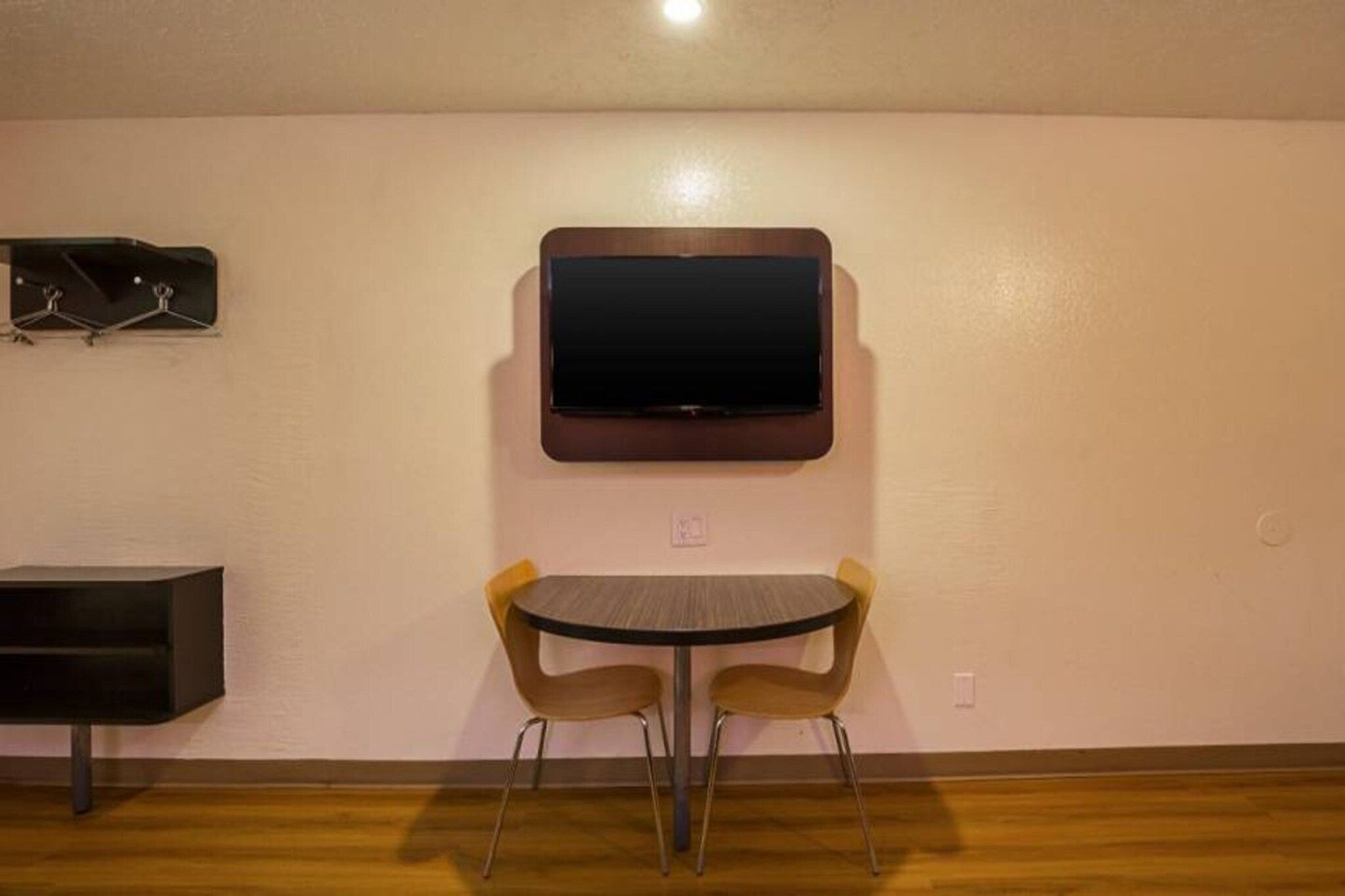A room with a flat-screen TV mounted on the wall, a small table with two chairs, and a black cabinet.