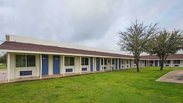 A row of motel buildings with individual rooms, a grassy lawn, and a tree.