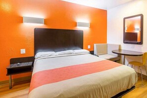 A hotel room with a bed, a desk, a chair, and a small table.