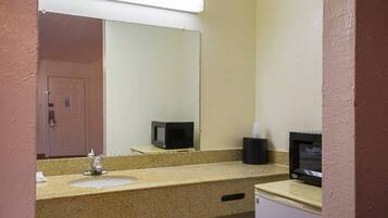 A bathroom with a sink, mirror, and a microwave on the countertop.