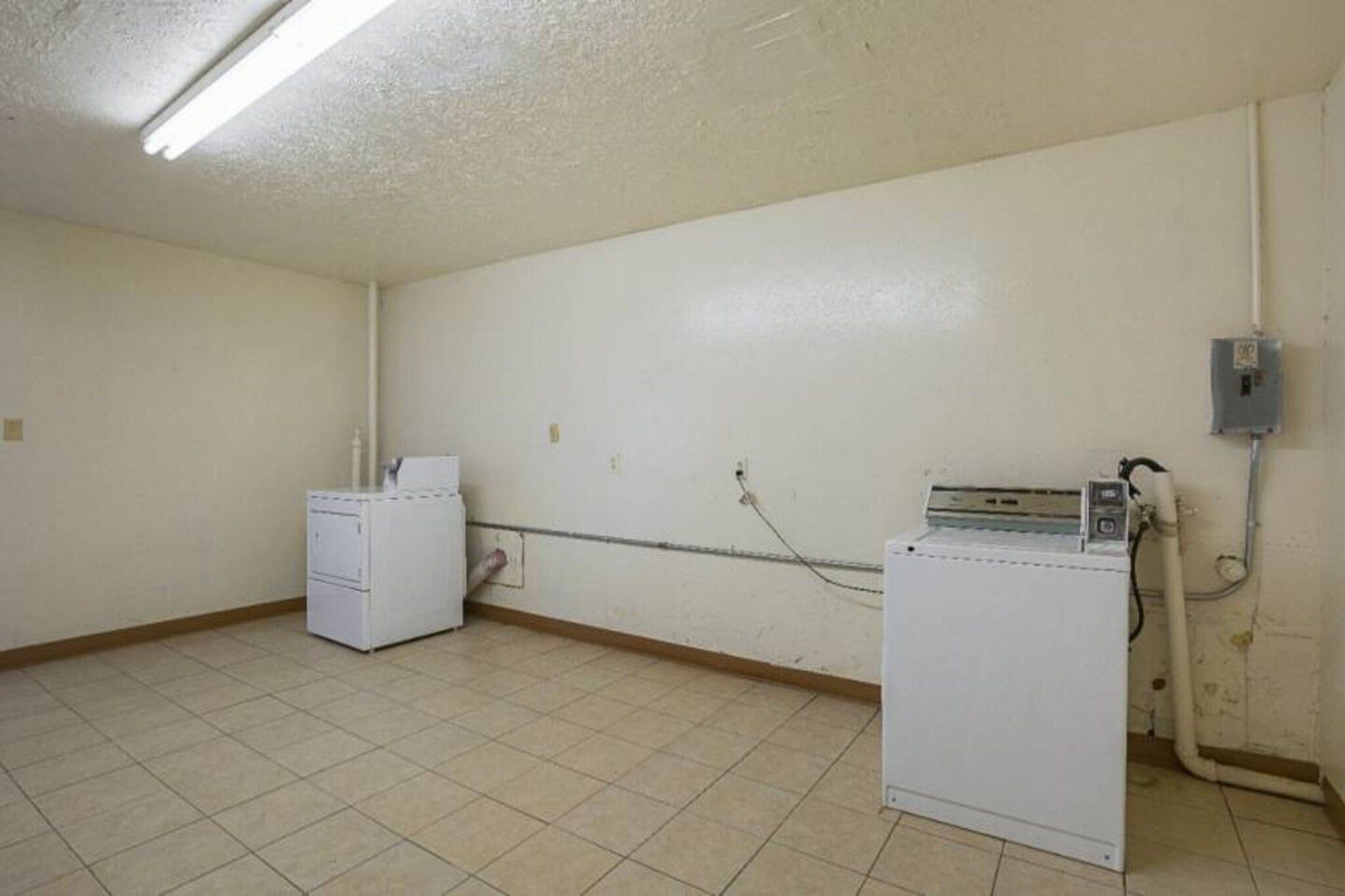 A laundry room with two white washing machines, a tiled floor, and a ceiling with fluorescent lighting.