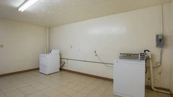 A laundry room with two white washing machines, a tiled floor, and a ceiling with fluorescent lighting.