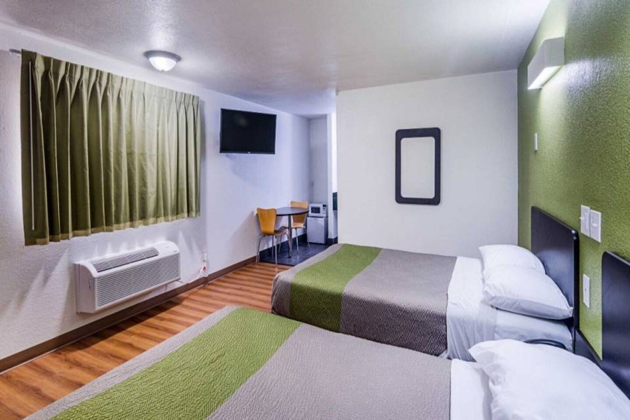 Habitació d'hotel amb dos llits, una taula petita amb cadires, un televisor i un aparell d'aire condicionat.