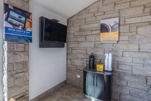 A small bathroom with a tiled floor, a mounted television, a cabinet with toiletries, and a poster on the wall.