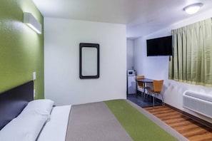 Quarto de hotel com cama, escrivaninha, cadeira, televisão e janela com cortinas.