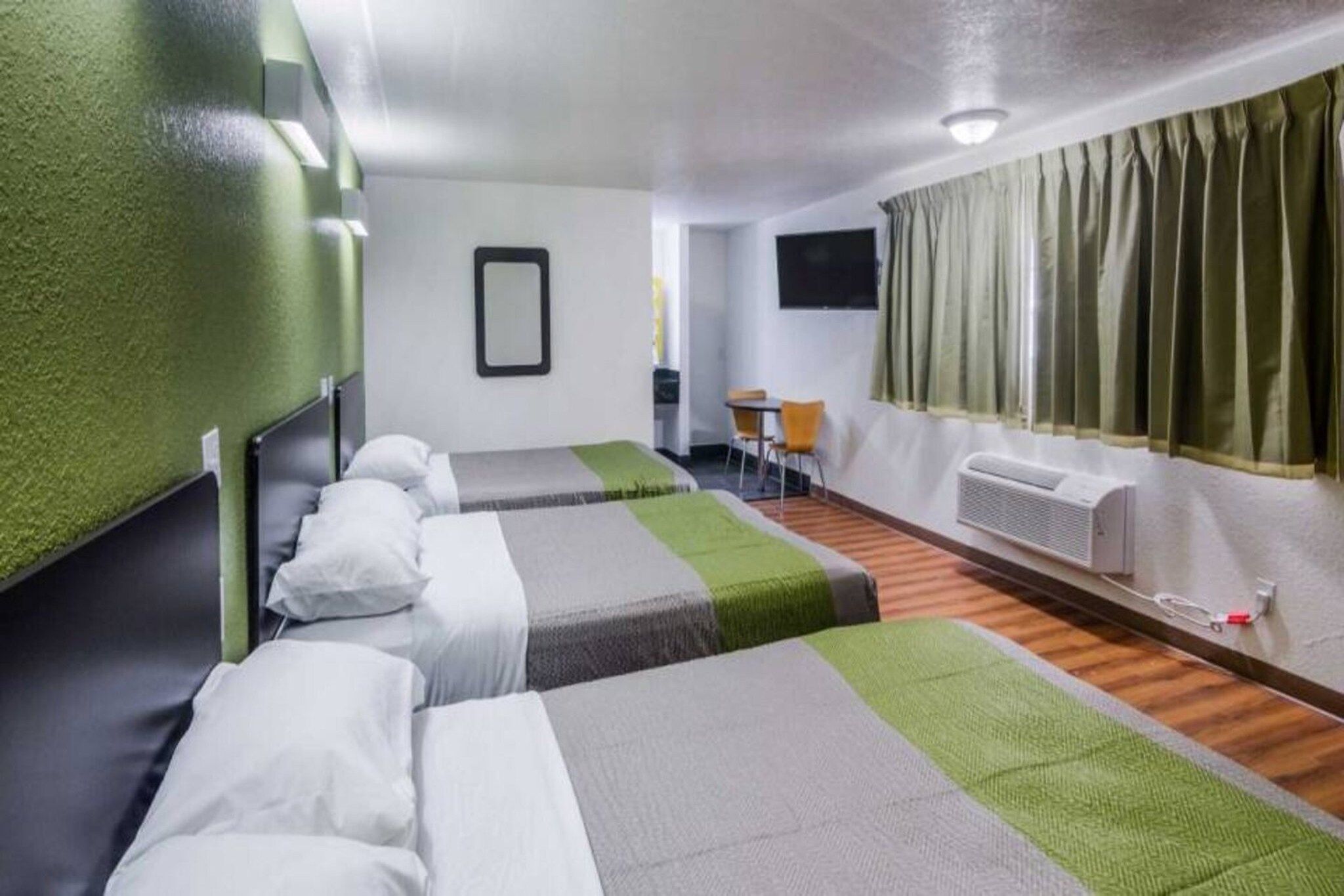 Habitació d'hotel amb dos llits, una taula petita, una cadira, una televisió i una finestra amb cortines.