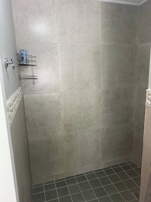 A bathroom with grey tiles, a metal rack with toiletries, and a tiled floor. - Stellenbosch On the Go! (Stellenbosch)