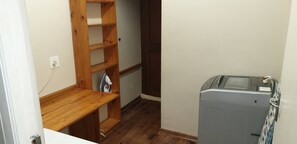 A small laundry room with a washing machine, a wooden shelf unit, and a power outlet. - Stellenbosch Holiday Home (Stellenbosch)